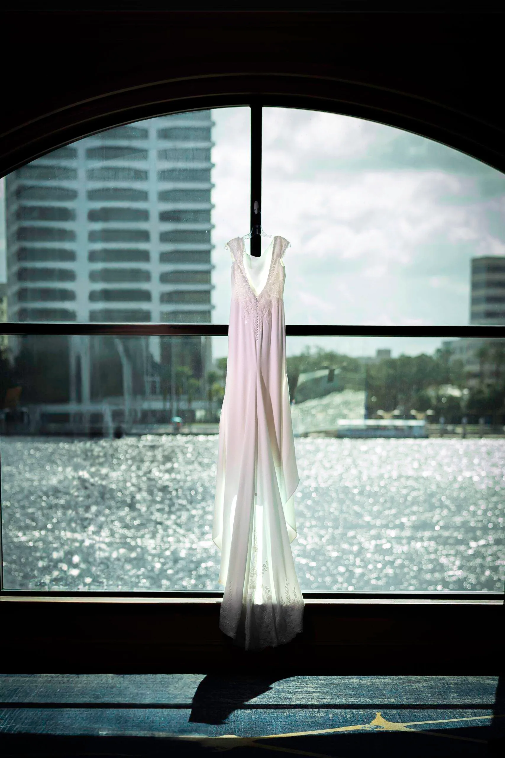A wedding dress hanging in front of a sunlit window.