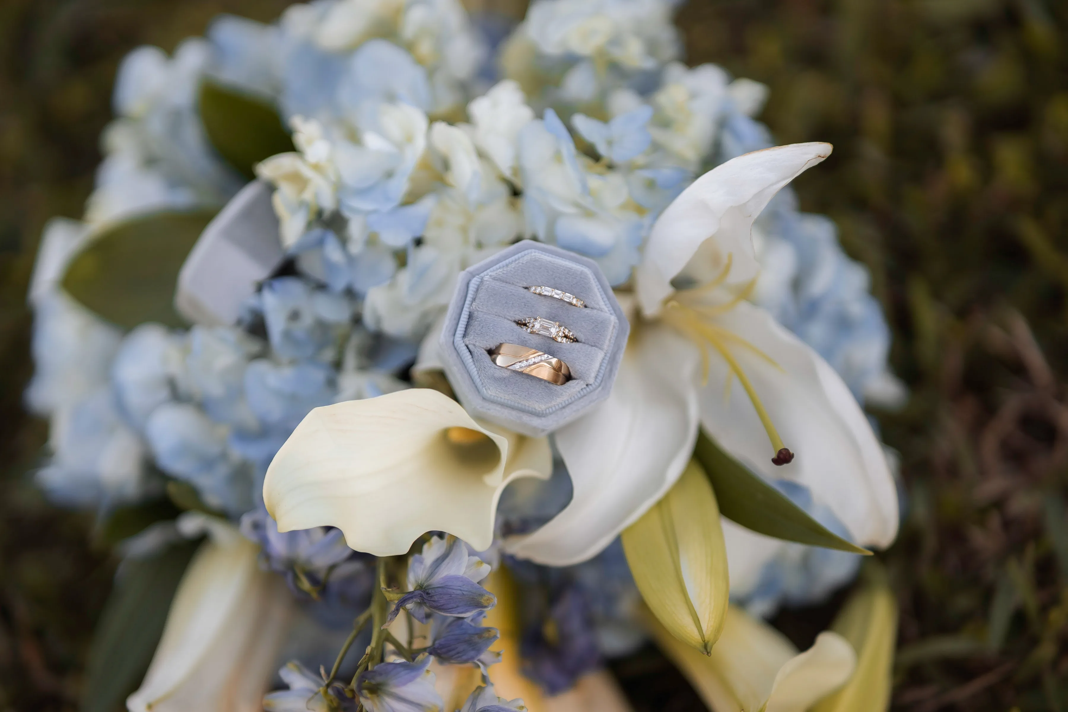 Wedding rings in an open gray ring box resting on a floral bouquet.