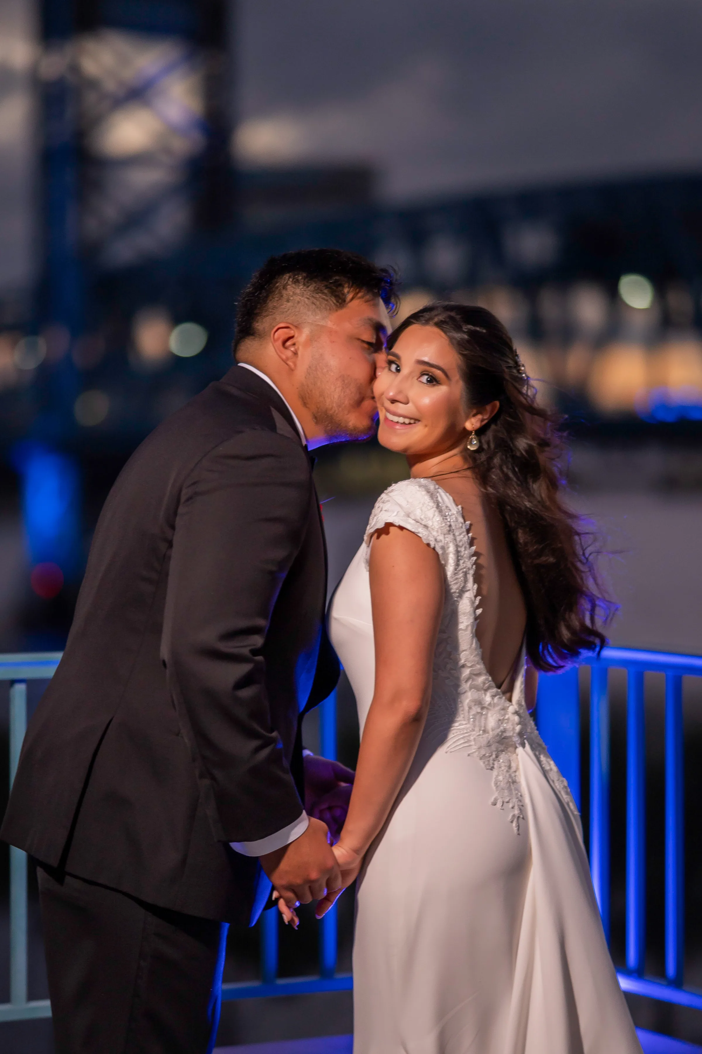 A bride and groom embracing against an evening backdrop with blue lights.