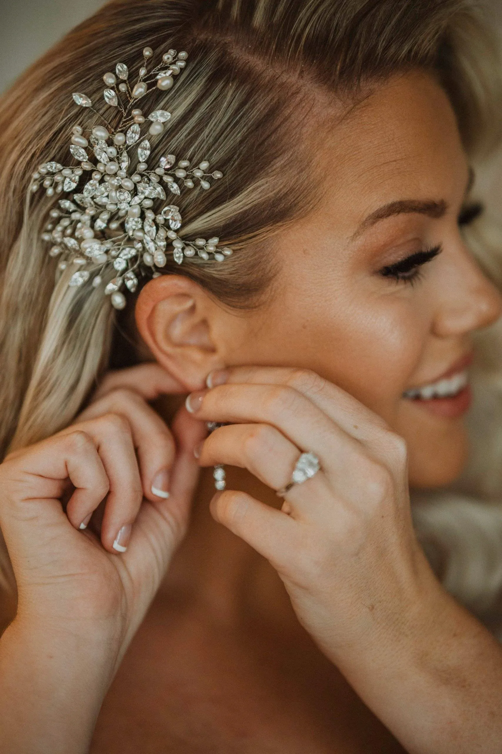 A smiling bride adjusting an earring beside a jeweled hair accessory.