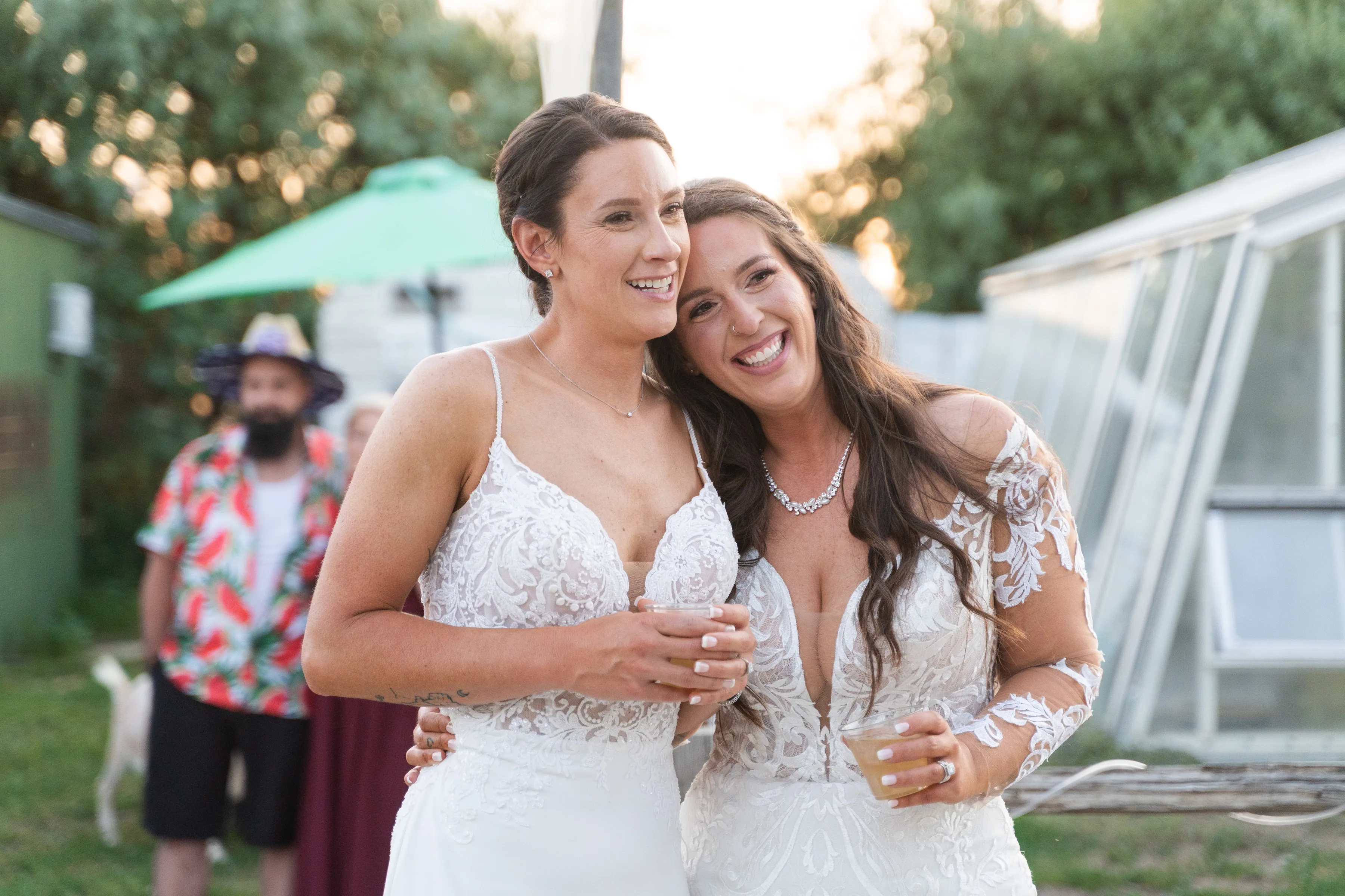 Two brides smiling together while holding drinks at an outdoor reception.