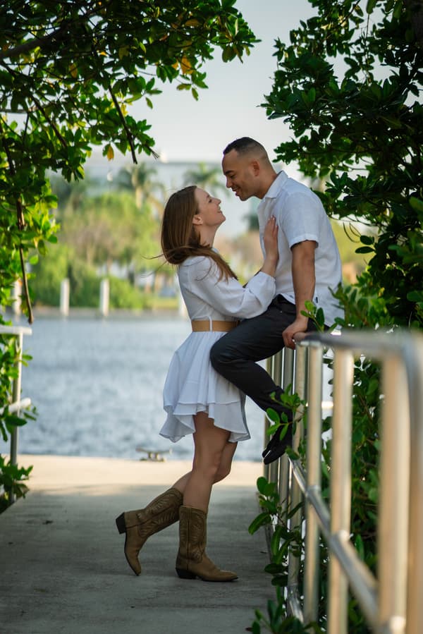A man and woman are kissing on a railing by the water.