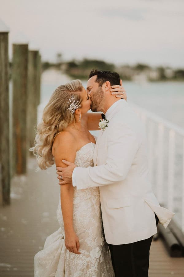 A man and woman are kissing on a pier with the ocean behind them.