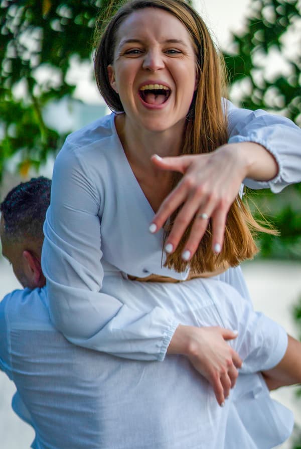 A woman is laughing while holding a man's face with her hands.