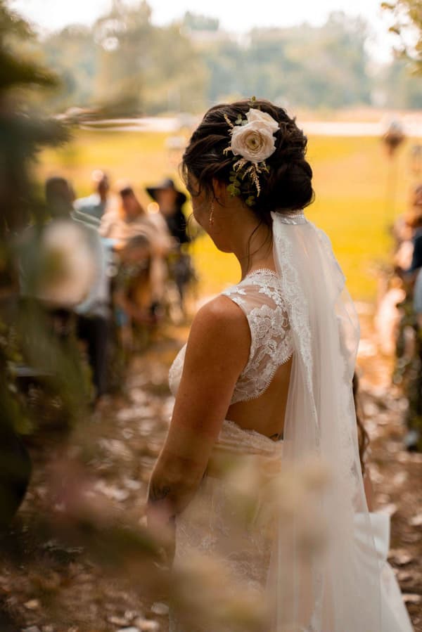 A bride wearing a white dress with a flower in her hair is walking down the street.