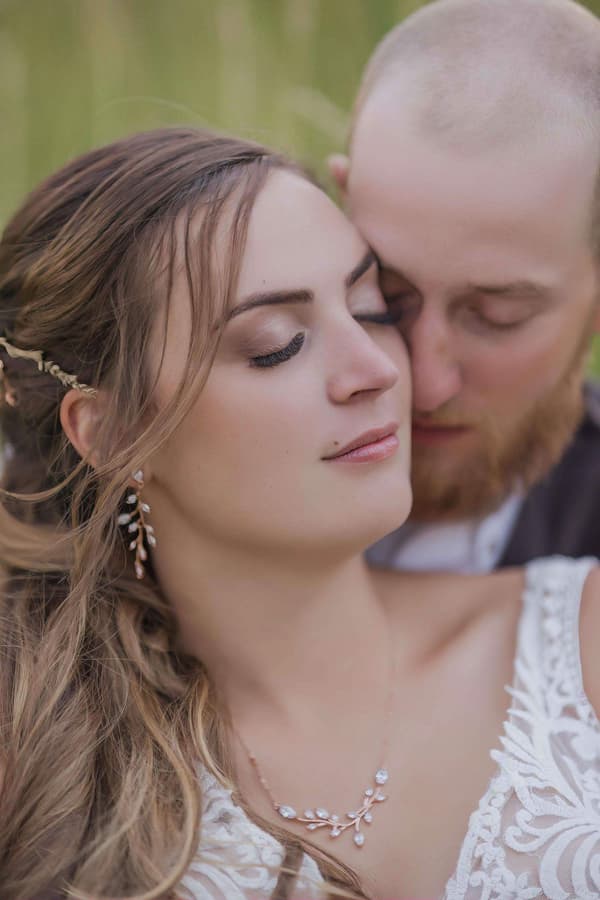 A woman with brown hair wearing a white dress is kissing a man on the cheek.