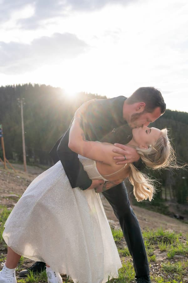 A man and a woman kissing with the sun behind them.