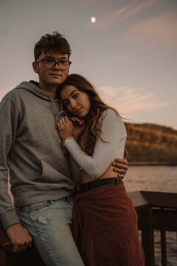 A man and a woman are hugging each other on the dock of a lake at sunset.